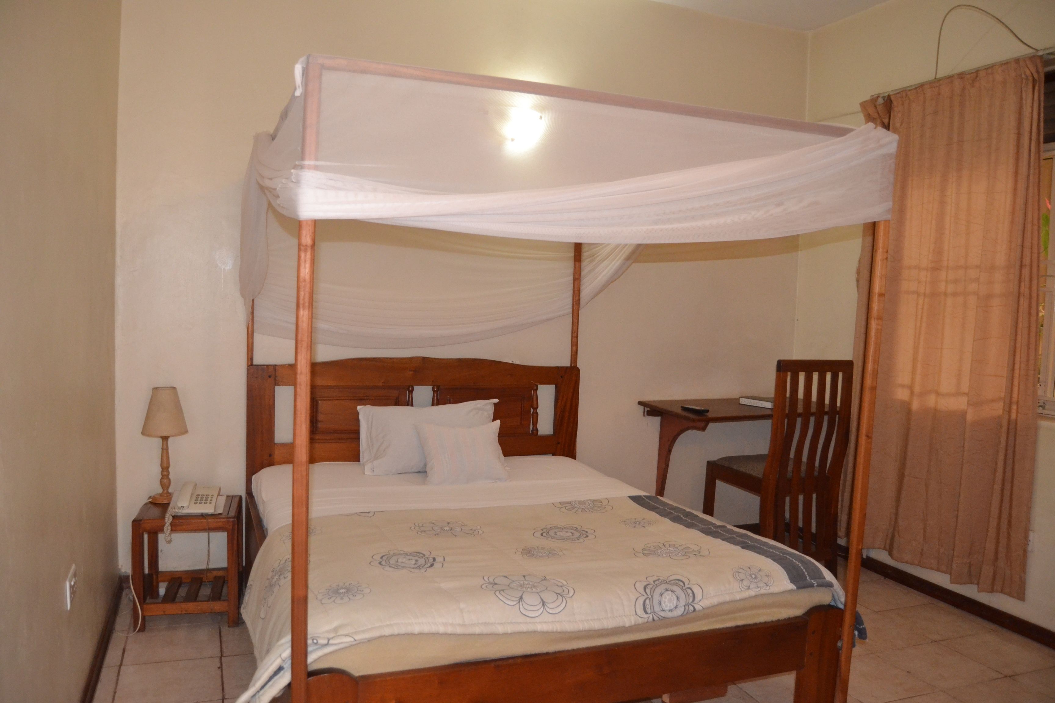A four-poster bed with a canopy, a bedside table with a lamp, a chair, and a desk with a chair.