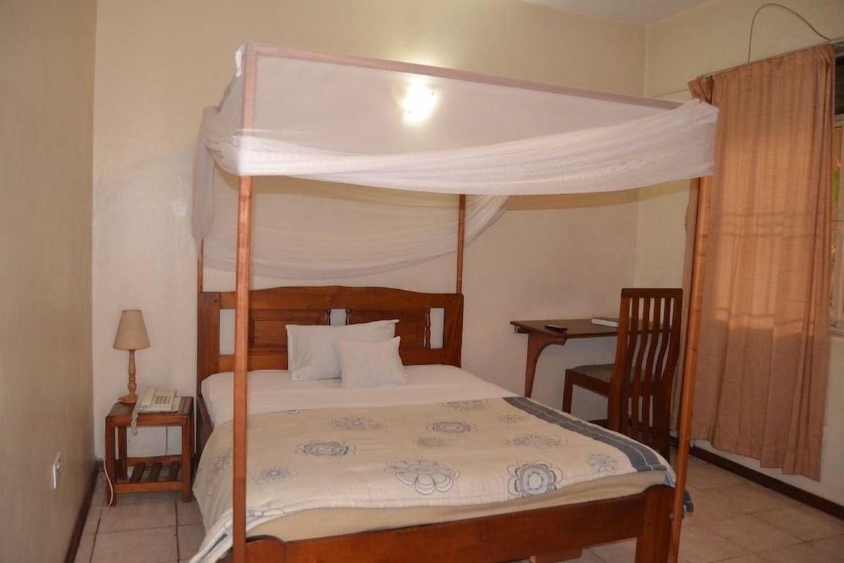 Una cama individual con dosel, una mesita de noche con lámpara y una silla.