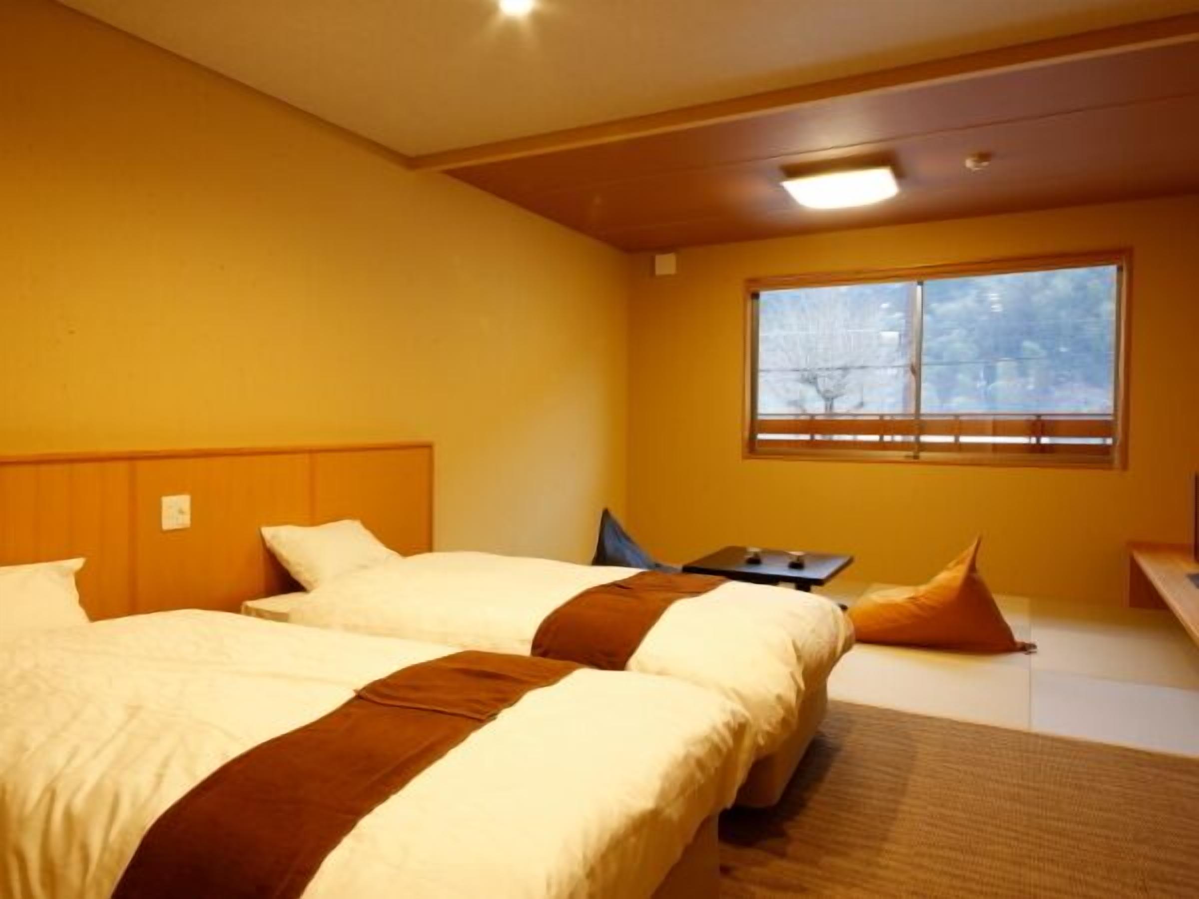 A hotel room with two beds, a small table, a window with a view, and a ceiling light.
