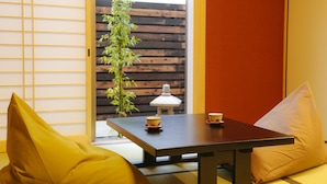 A room with a wooden table, two yellow cushions, a white lamp, and a wooden fence outside. - Fugetsugyosho (Toyooka)