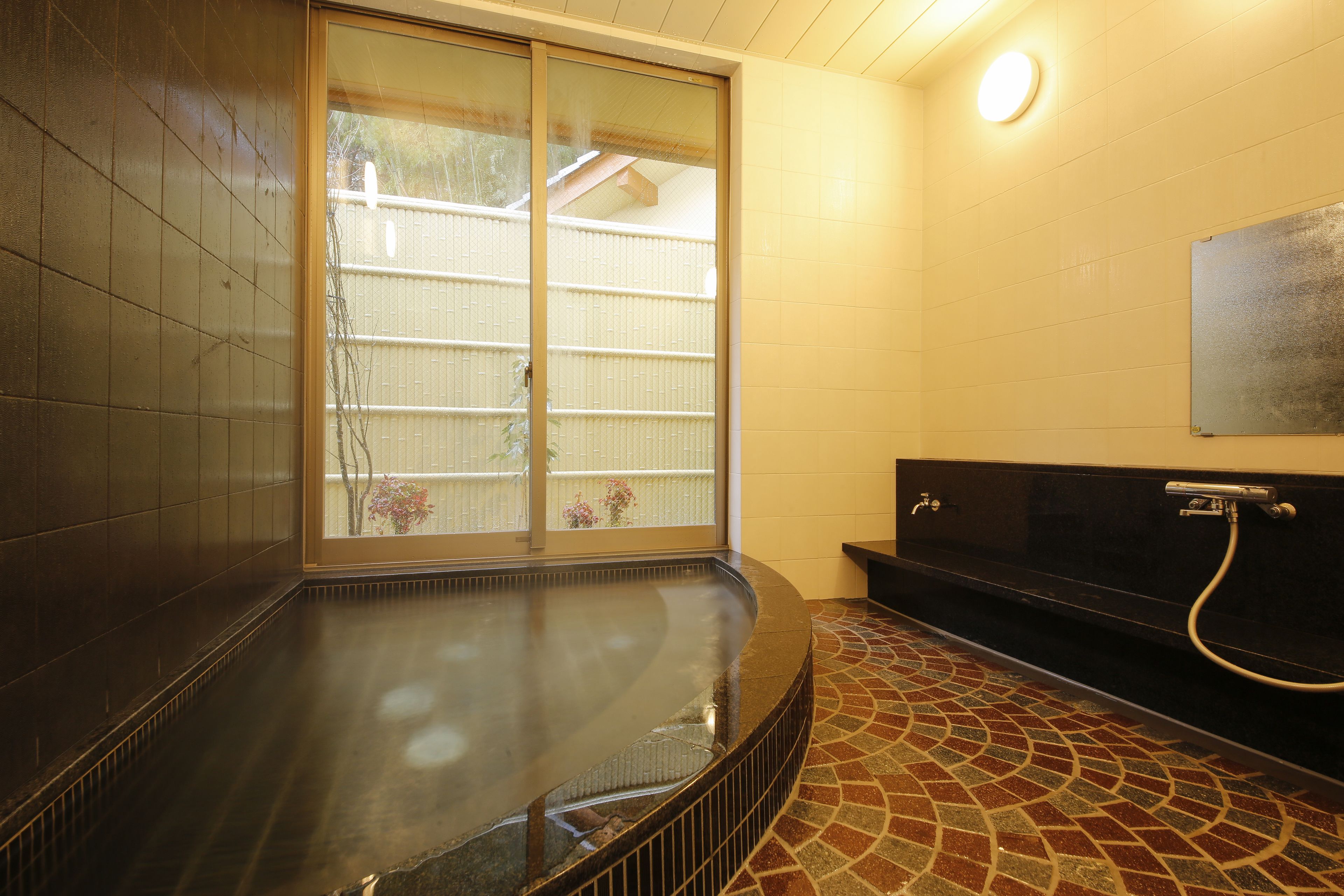 A traditional Japanese-style bath with a sliding glass door, a tiled floor, and a black bench.