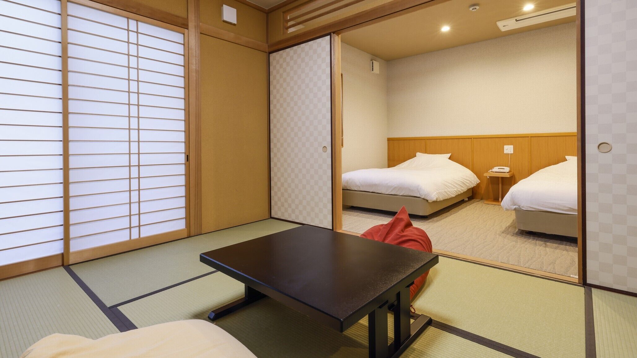 A traditional Japanese room with tatami flooring, a low table, and two beds.
