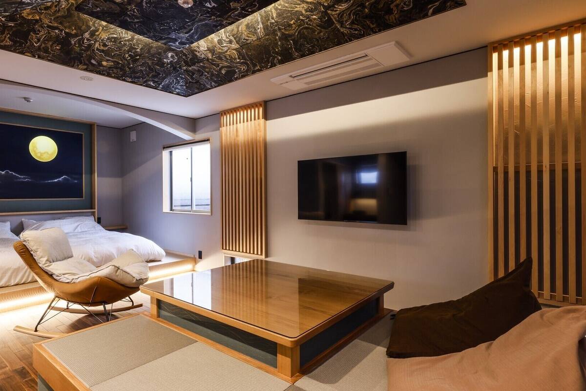 Quarto de hotel moderno com cama, sofá, mesa de centro, televisão e teto com design semelhante a mármore.
