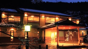 A traditional Japanese building with multiple illuminated windows and a covered entrance. - Fugetsugyosho (Toyooka)