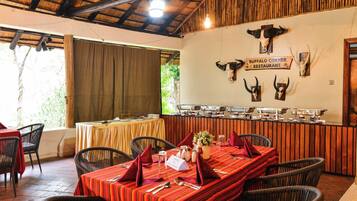A restaurant with a thatched roof, wooden beams, and a buffet counter.