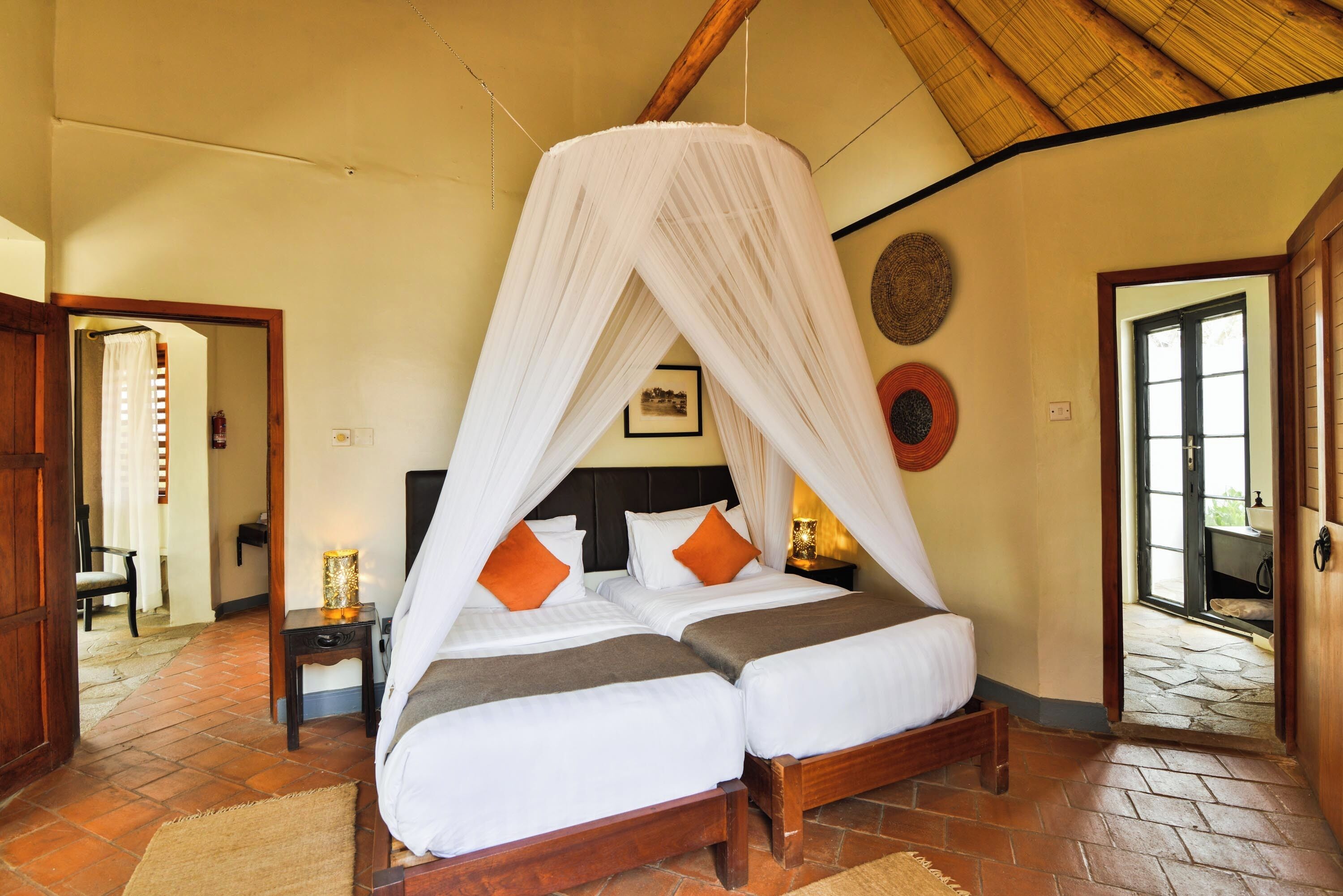 A room with a bed under a canopy, a nightstand with a lamp, a picture on the wall, and a door leading outside.
