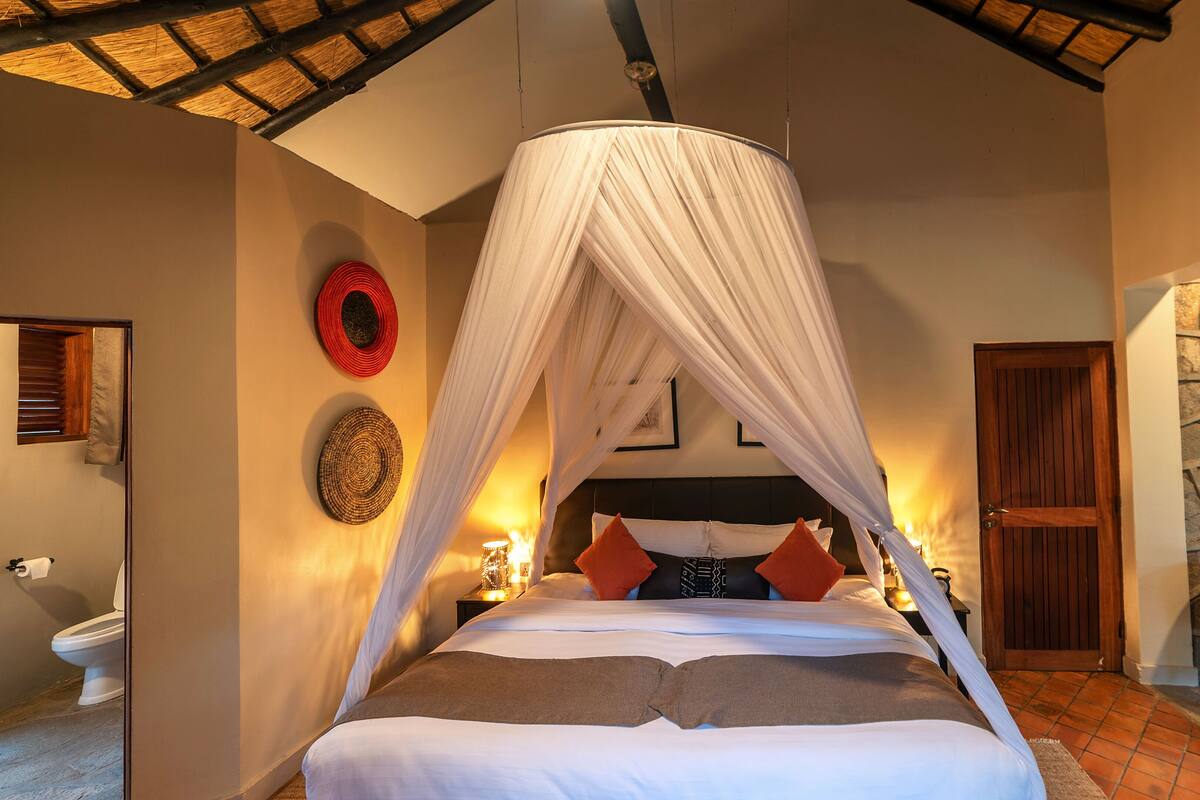 Quarto com cama de dossel, parede de pedra, cadeira estampada com padrão de zebra e porta de madeira.