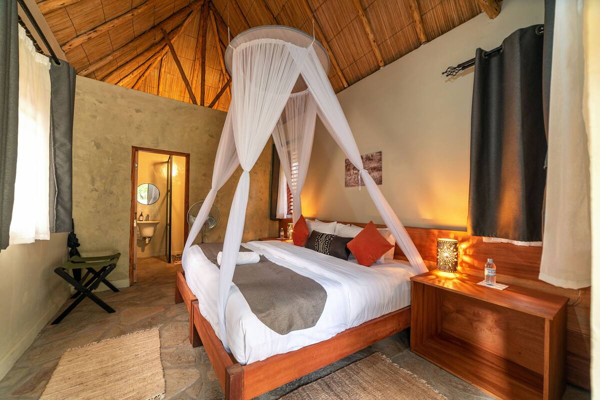 Um quarto com cama de madeira, mesa de cabeceira, criadeira com abajur e cama com dossel.