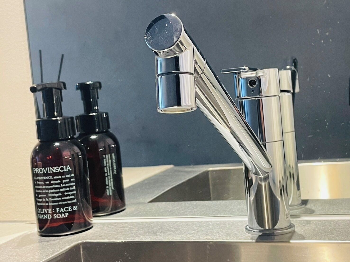 A modern bathroom with a chrome faucet, a mirror, and two bottles of Provinscia olive face and hand soap.