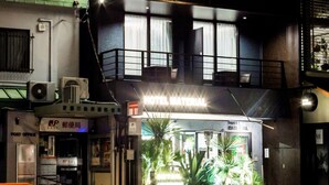 A hotel with a prominent 'M' sign, a ground-level entrance with plants, and a rooftop terrace with string lights. - Hotel Material (Kyoto)