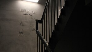 A staircase with a metal railing leading to a landing. The wall above the stairs has a sign indicating hotel material, floor map, and room details. - Hotel Material (Kyoto)