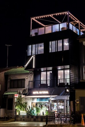 A hotel with a modern design, featuring a prominent 'HOTEL MATERIAL' sign, large windows, and a balcony with string lights. - Hotel Material (Kyoto)