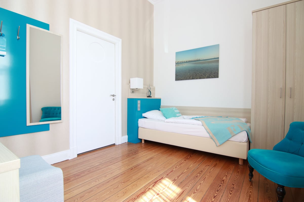 Een slaapkamer met een bed, een stoel, een kledingkast, een spiegel en een schilderij aan de muur.