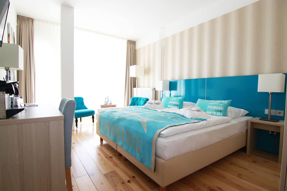 Een hotelkamer met een bed, een bureau, een stoel en uitzicht op zee.