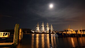 Une scène nocturne d’un port, avec un navire amarré à un quai, illuminé par un éclairage d’ambiance.