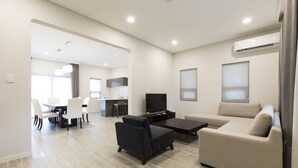 A modern living room with a sofa, a coffee table, and a TV. There is a dining area with chairs and a table. - Pacific Palm Resort (Saipan)