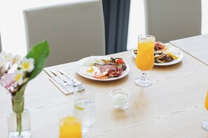 Une table à manger avec des assiettes remplies de nourriture et des boissons, un vase de fleurs et une fenêtre avec des rideaux.