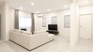 A modern living room with a sofa, TV, and air conditioning unit. - Pacific Palm Resort (Saipan)