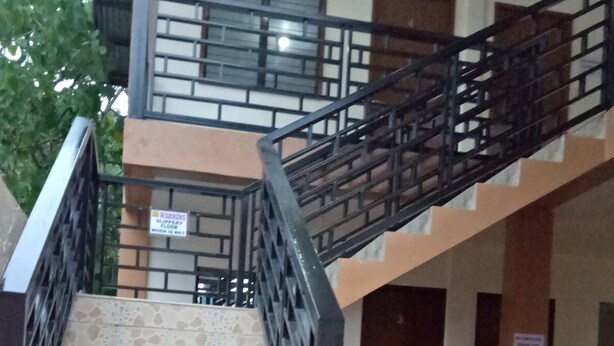 Uma escadaria com corrimão de metal preto que leva a um nível superior. Há plantas em vasos na base da escada.
