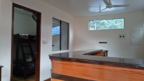 Cozinha com bancada de madeira, ventoinha no teto, janela e porta que dá para outro cômodo.