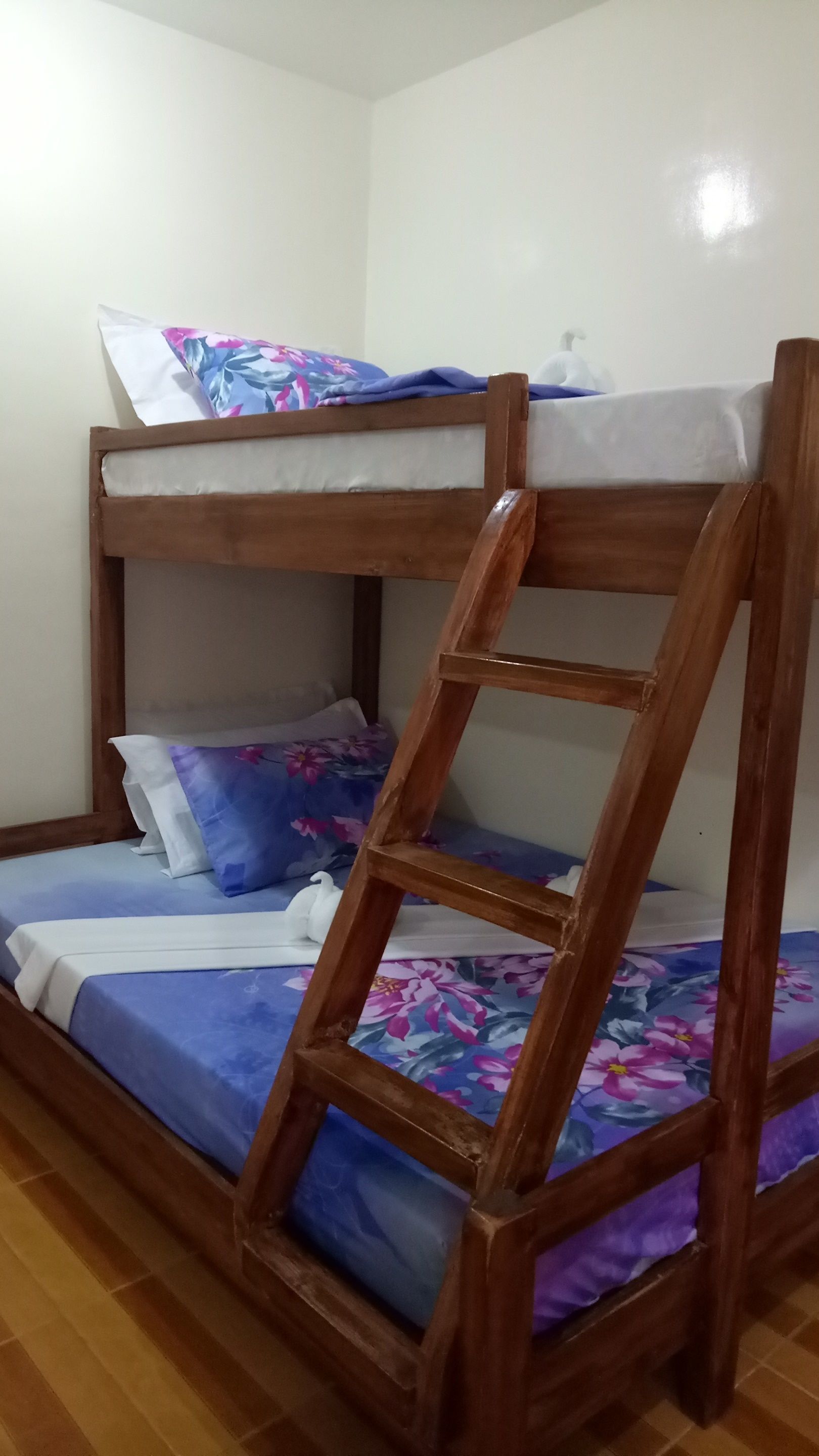 Un lit superposé avec une échelle en bois, une literie bleue et des oreillers à motifs floraux.