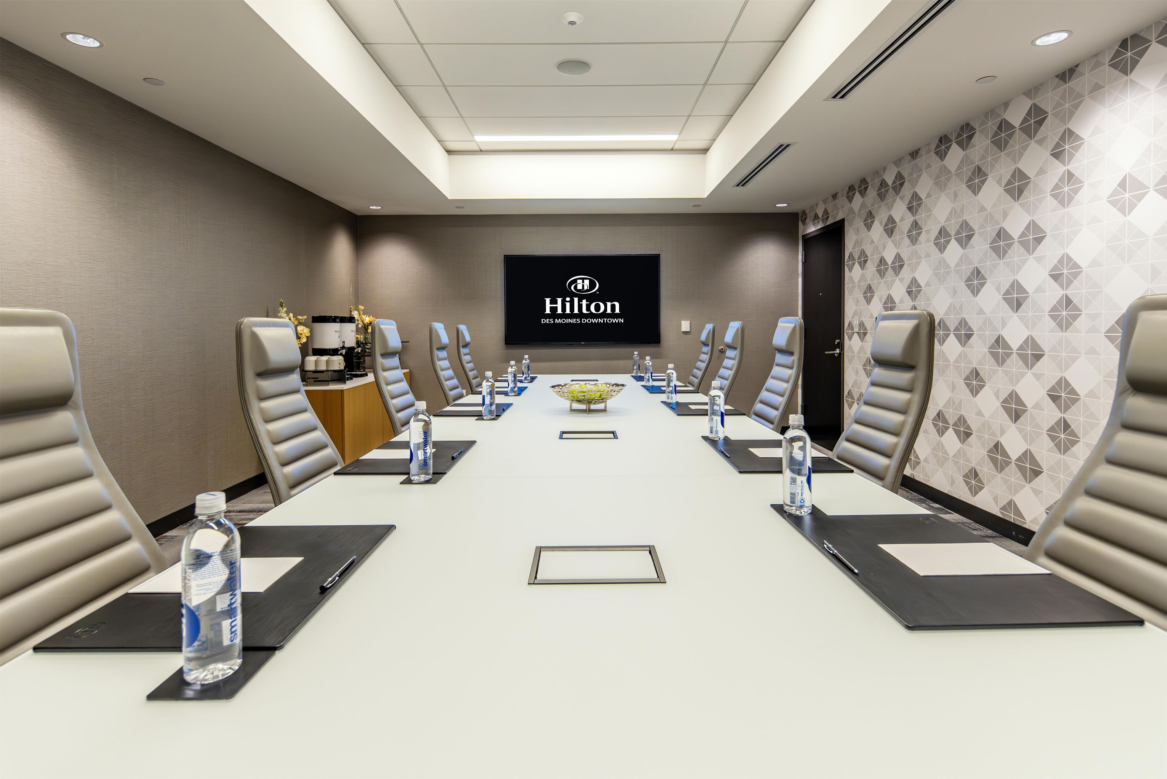 A conference room with a long table, chairs, water bottles, and a coffee station.