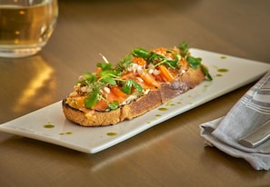 A rectangular white plate with a slice of toasted bread topped with salmon, greens, and a drizzle of olive oil. - Hilton Des Moines Downtown (Des Moines)