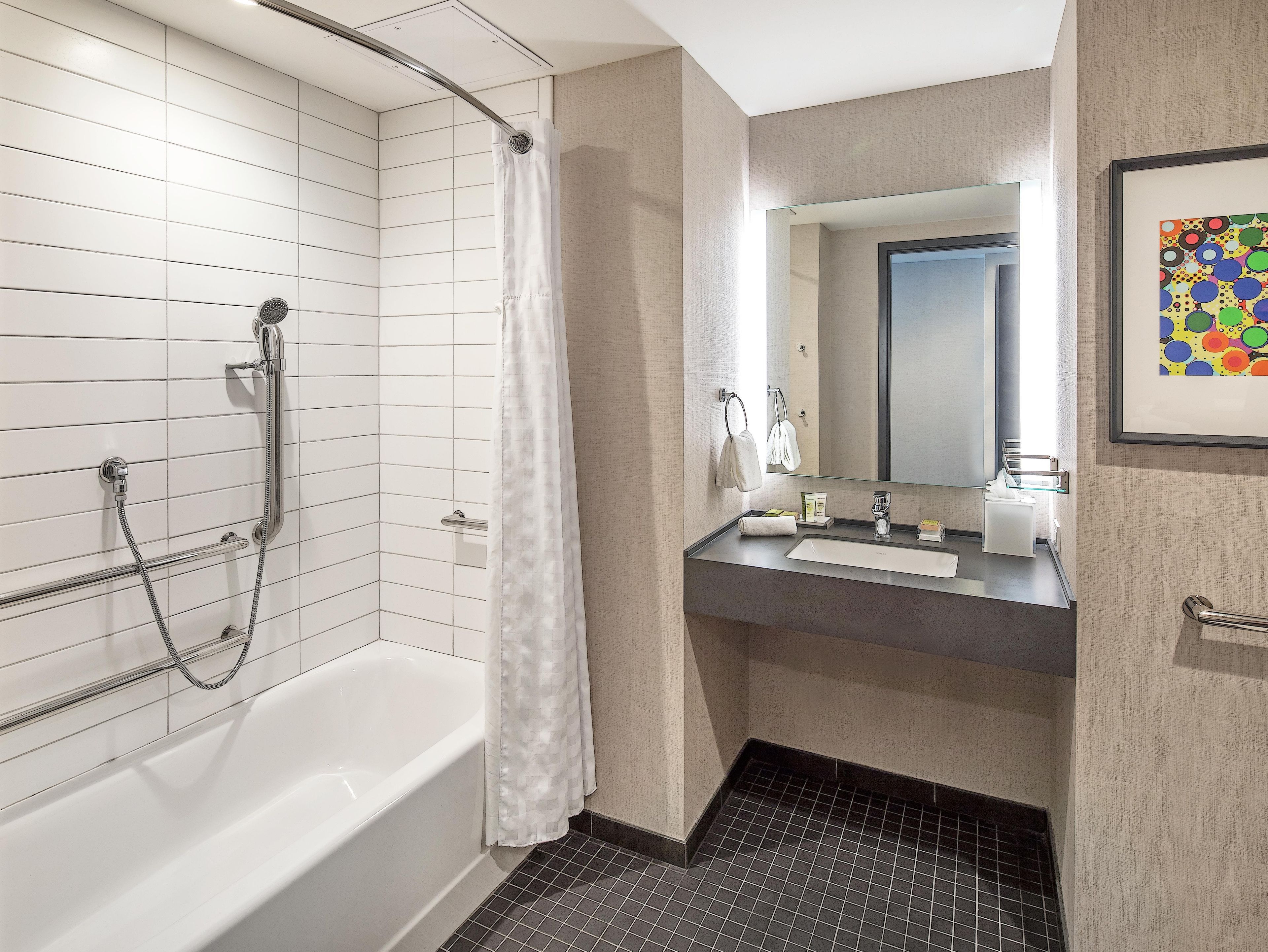 A modern bathroom with a white bathtub, a shower with a curved glass door, a vanity with a mirror, and a tiled floor.
