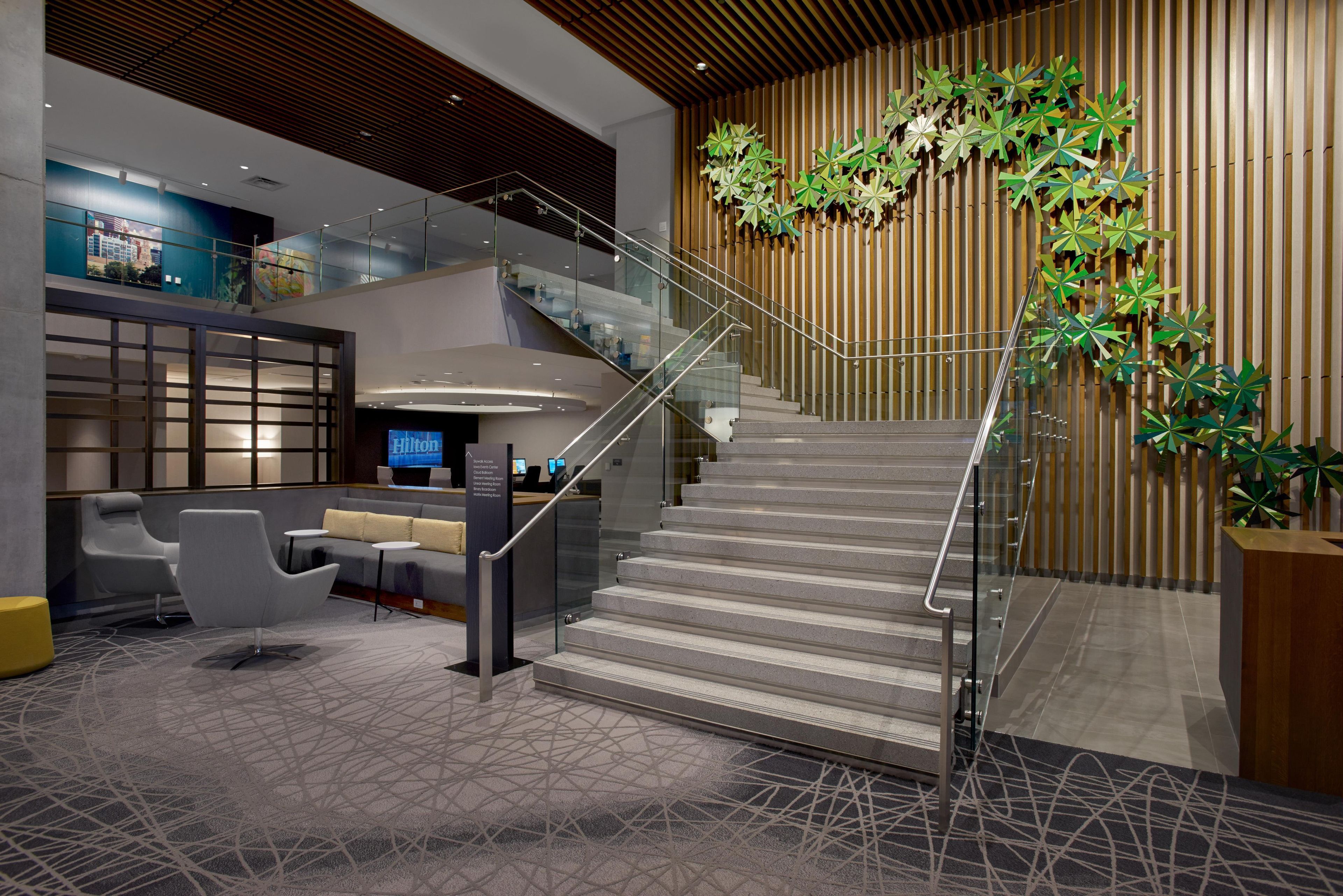 A hotel lobby with a staircase, seating area, and a digital display.