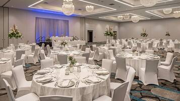 A banquet hall with round tables, white chairs, and chandeliers.
