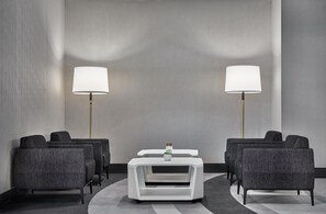 Habitación de hotel con zona de estar, dos lámparas de pie y una mesita con un florero.