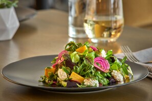 A plate of mixed greens and vegetables on a table with a glass of white wine in the background. - Hilton Des Moines Downtown (Des Moines)