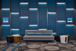 A modern hotel room with a grey sofa, two side tables, a patterned carpet, and a wall with illuminated panels. - Hilton Des Moines Downtown (Des Moines)