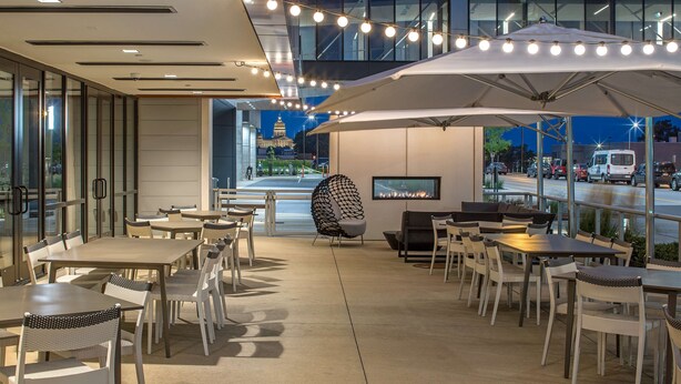 An outdoor dining area with tables and chairs, a large umbrella, and a TV screen.