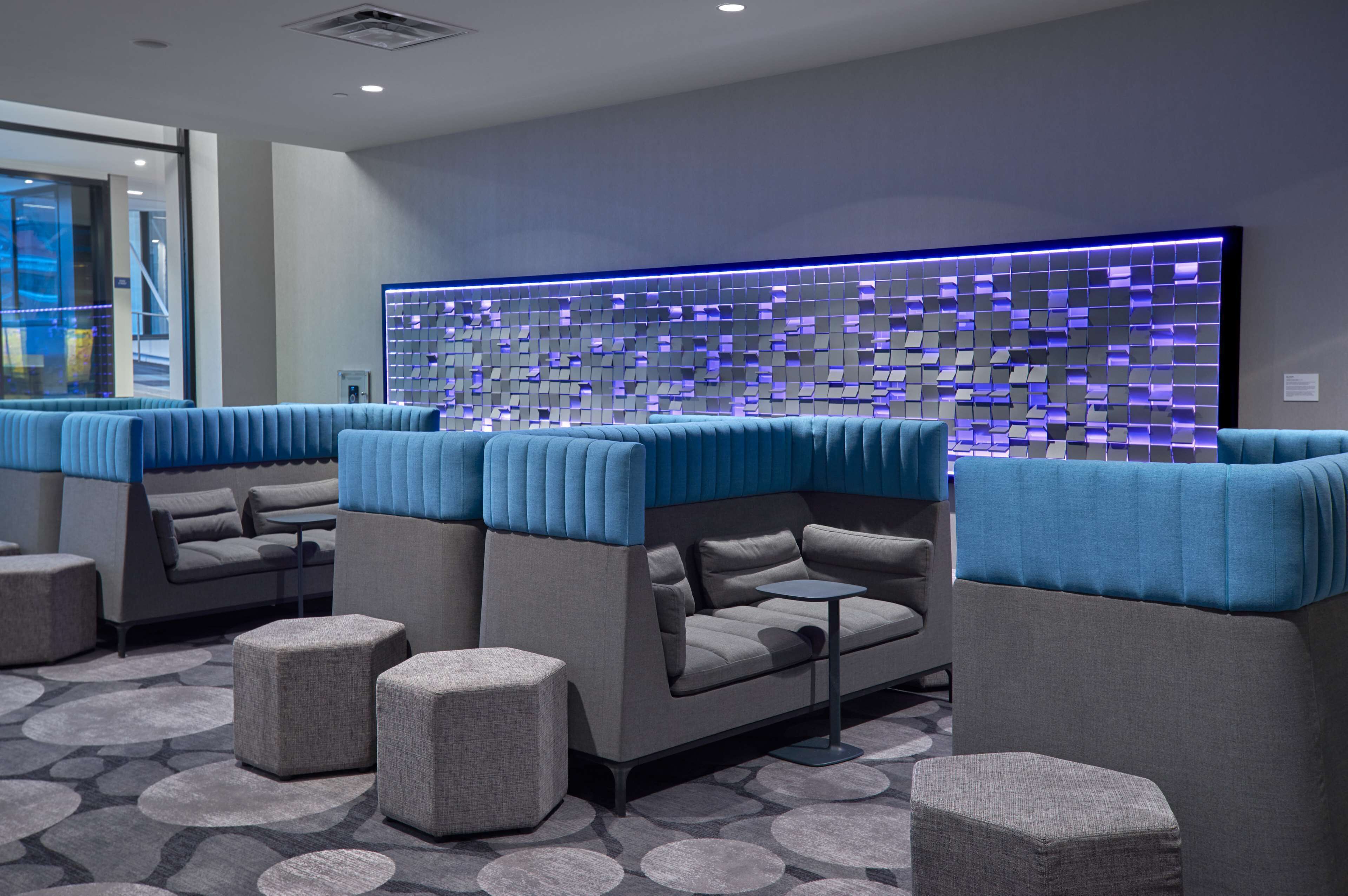 Un área de lounge moderna con una disposición de sofás y otomanas, una pared con diseño y una alfombra estampada.