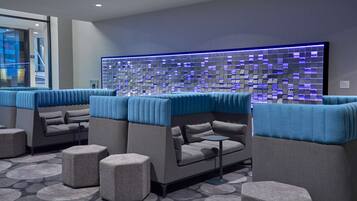 Un área de lounge moderna con una disposición de sofás y otomanas, una pared con diseño y una alfombra estampada.