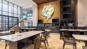 A modern restaurant with a large, abstract wall art piece, multiple seating areas, and a staircase leading to an upper level.