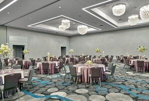 Un amplio salón de conferencias con mesas redondas, sillas y una alfombra estampada.