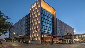 A modern hotel with a prominent 'Hilton' sign, large windows, and a covered outdoor area with seating.