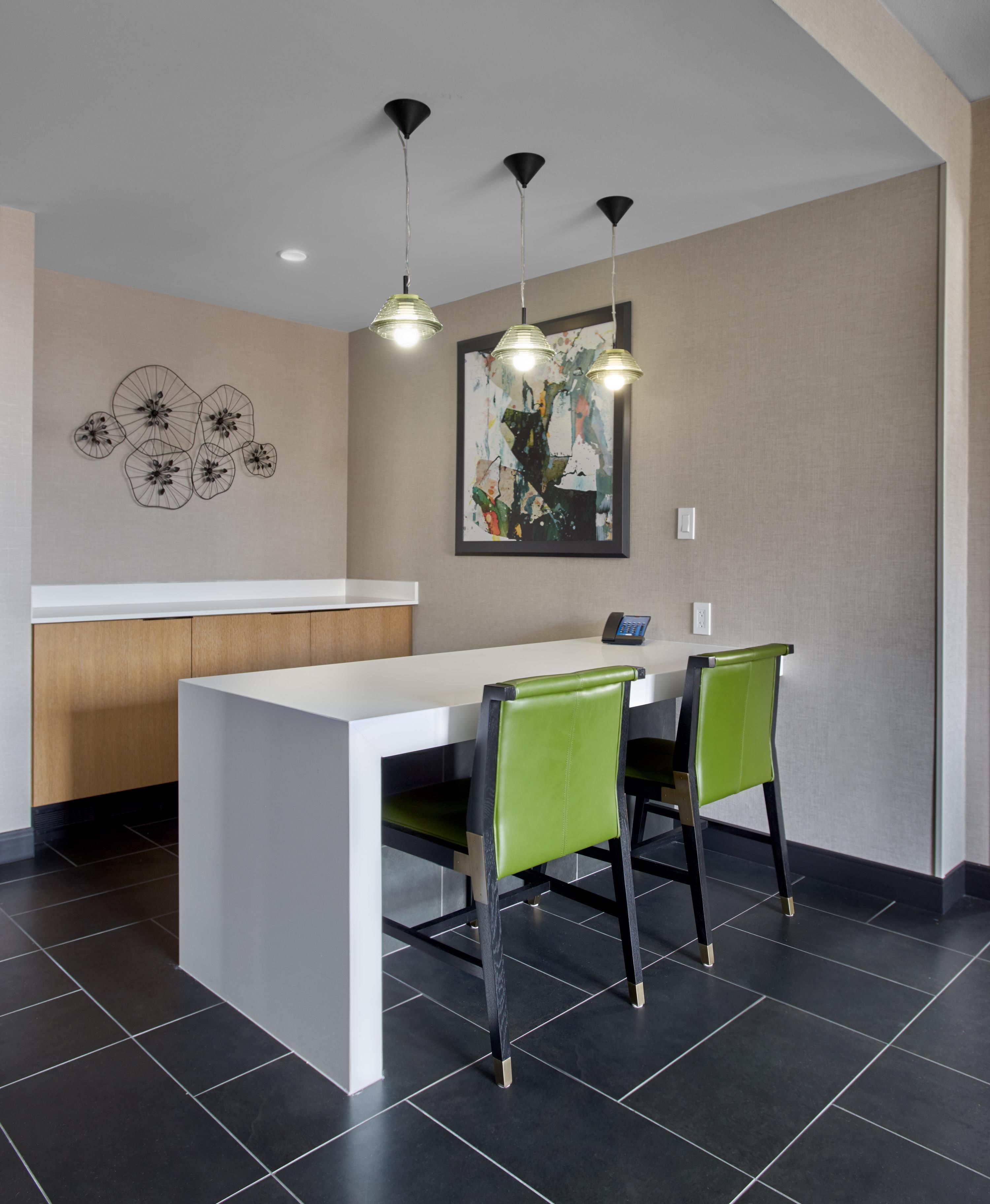A modern kitchen with a white countertop, black chairs, and pendant lights.