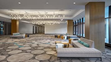 Een ruime lobby met een patroonloos tapijt, zitgedeeltes en een moderne kroonluchter.