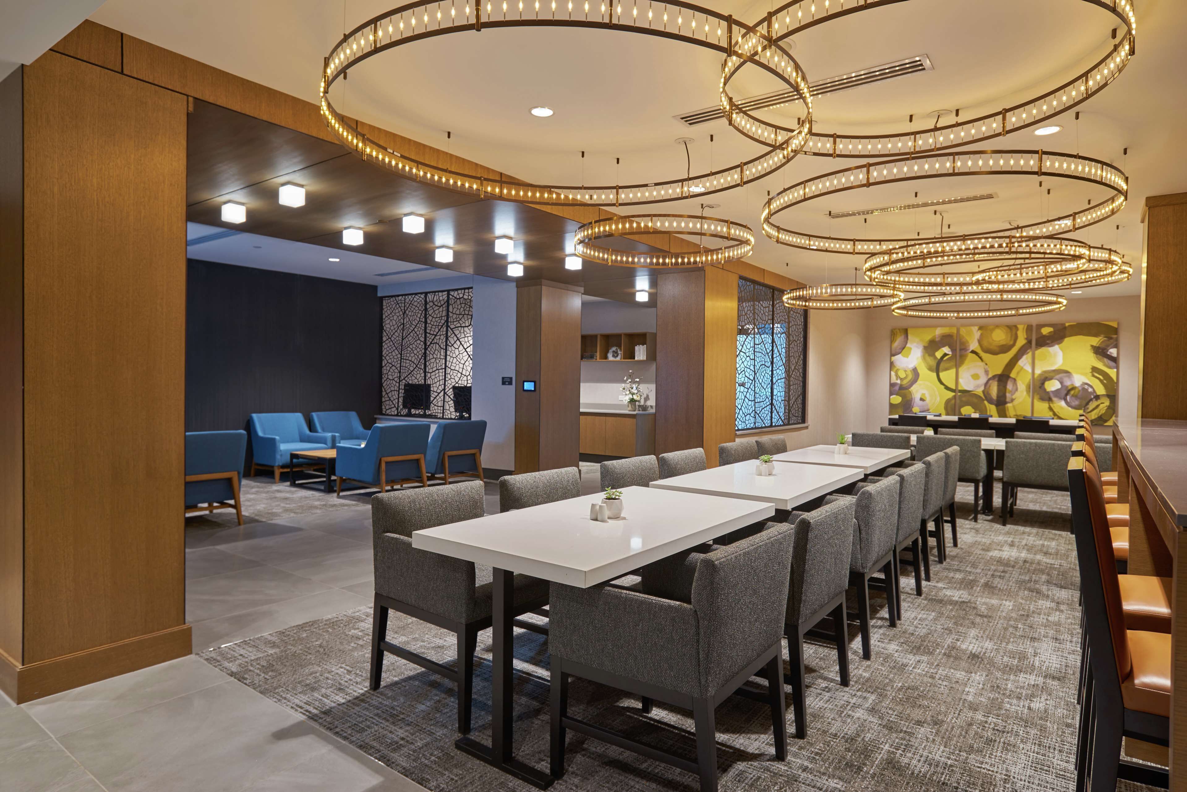 A modern hotel lobby with a long dining area, blue seating, and a large abstract painting.