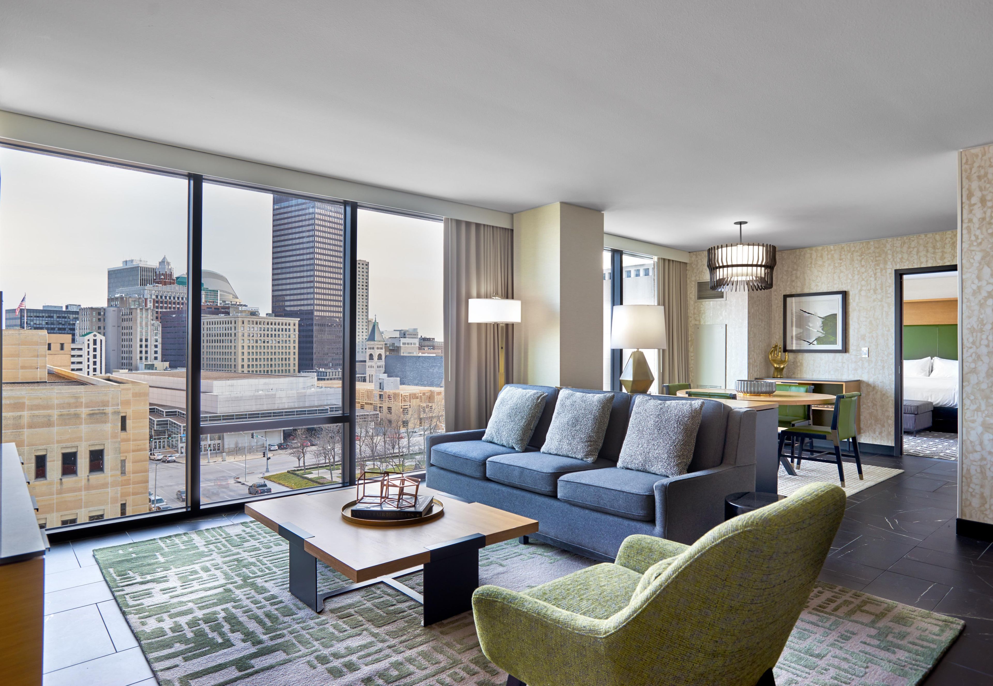 Quarto de hotel moderno com vista para a cidade, um sofá, uma cadeira, uma escrivaninha e um espaço de jantar.