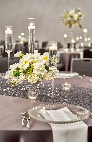 A table set with white flowers, candles, and silverware, suggesting a formal dining setting. - Hilton Des Moines Downtown (Des Moines)