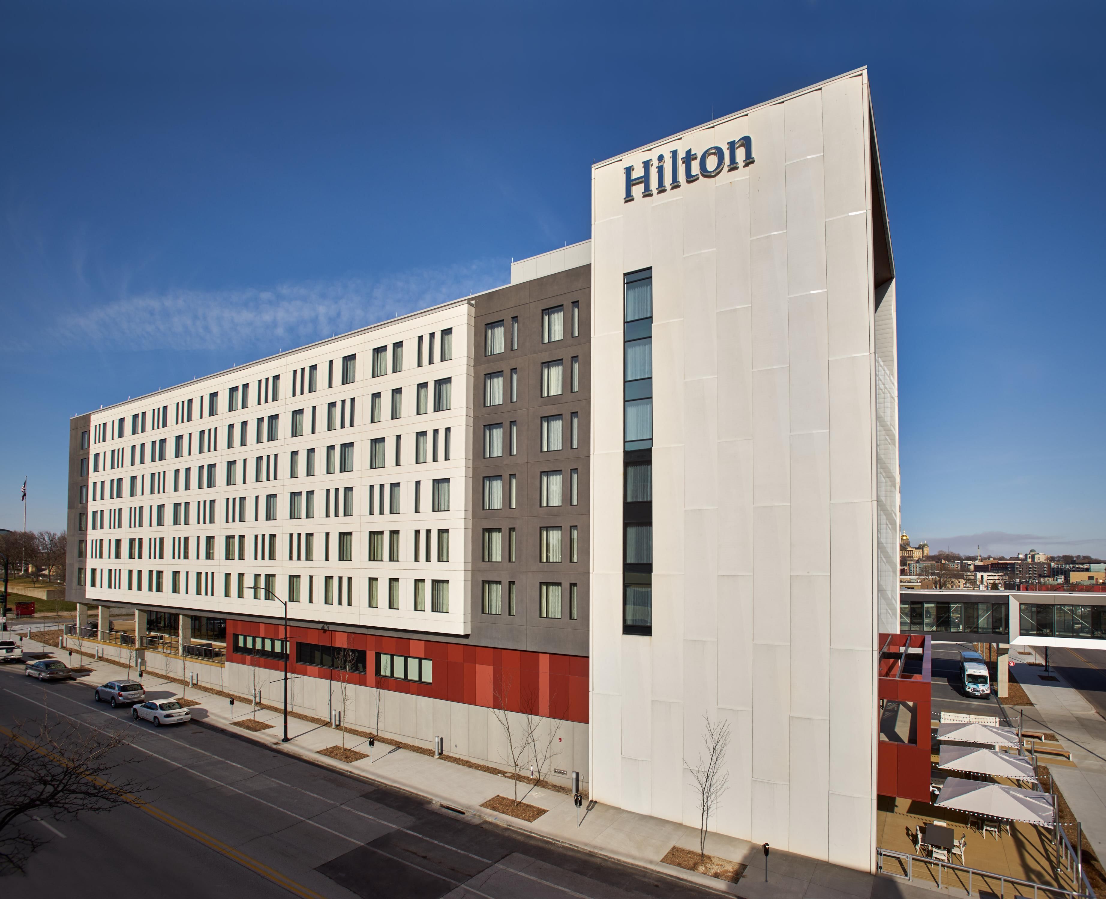 A modern hotel building with a prominent 'Hilton' sign, multiple floors, and a parking area with a bus stop.