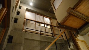 Una escalera con barandilla de madera y balaustres de metal, que lleva a una habitación con piso de concreto y techo de madera.