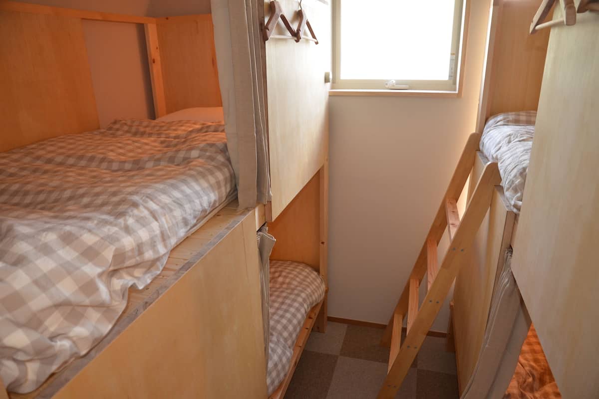 A dormitory-style room with bunk beds, a window, and a door.
