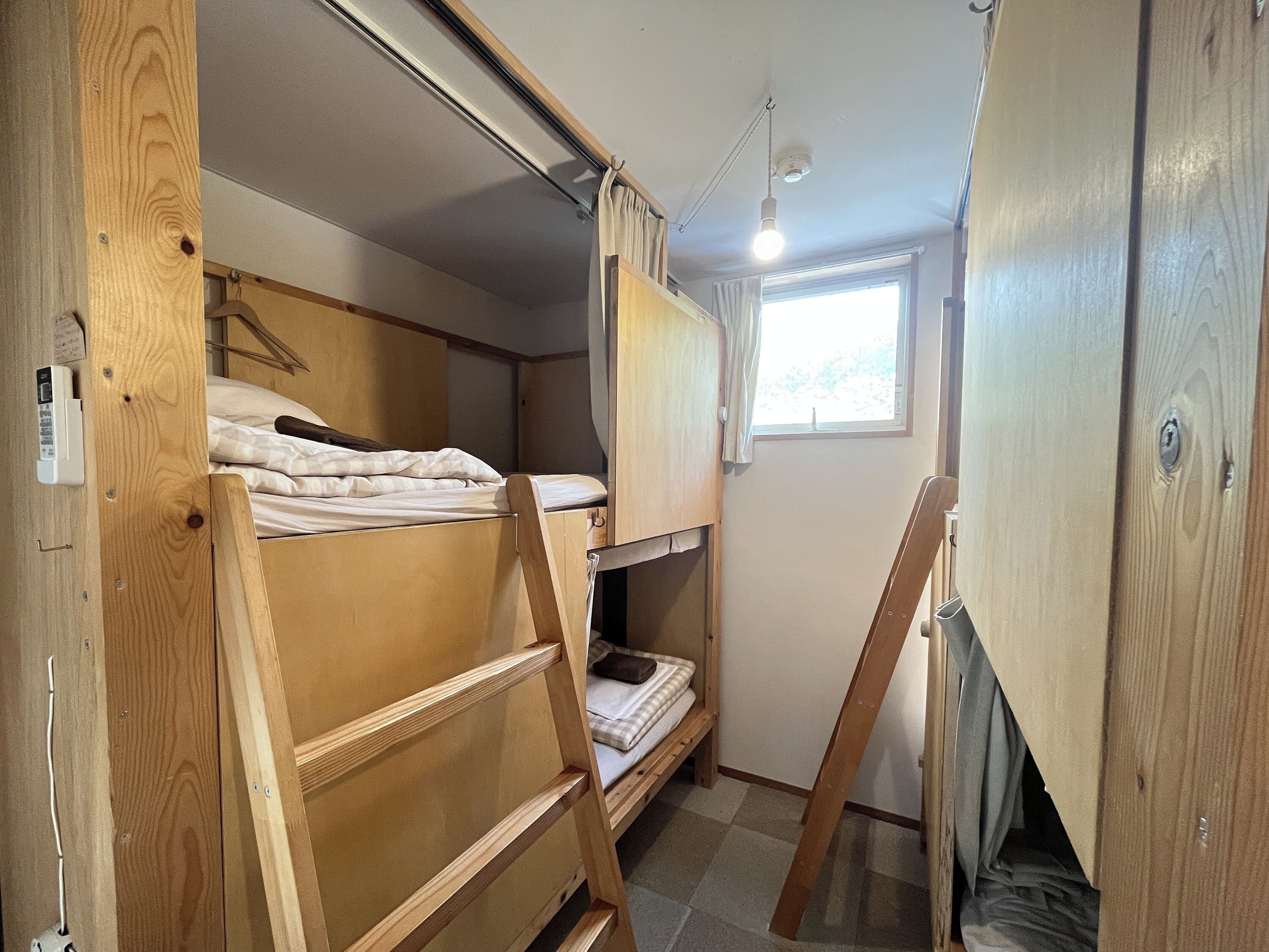 Habitación pequeña con literas, una ventana y una lámpara en el techo.