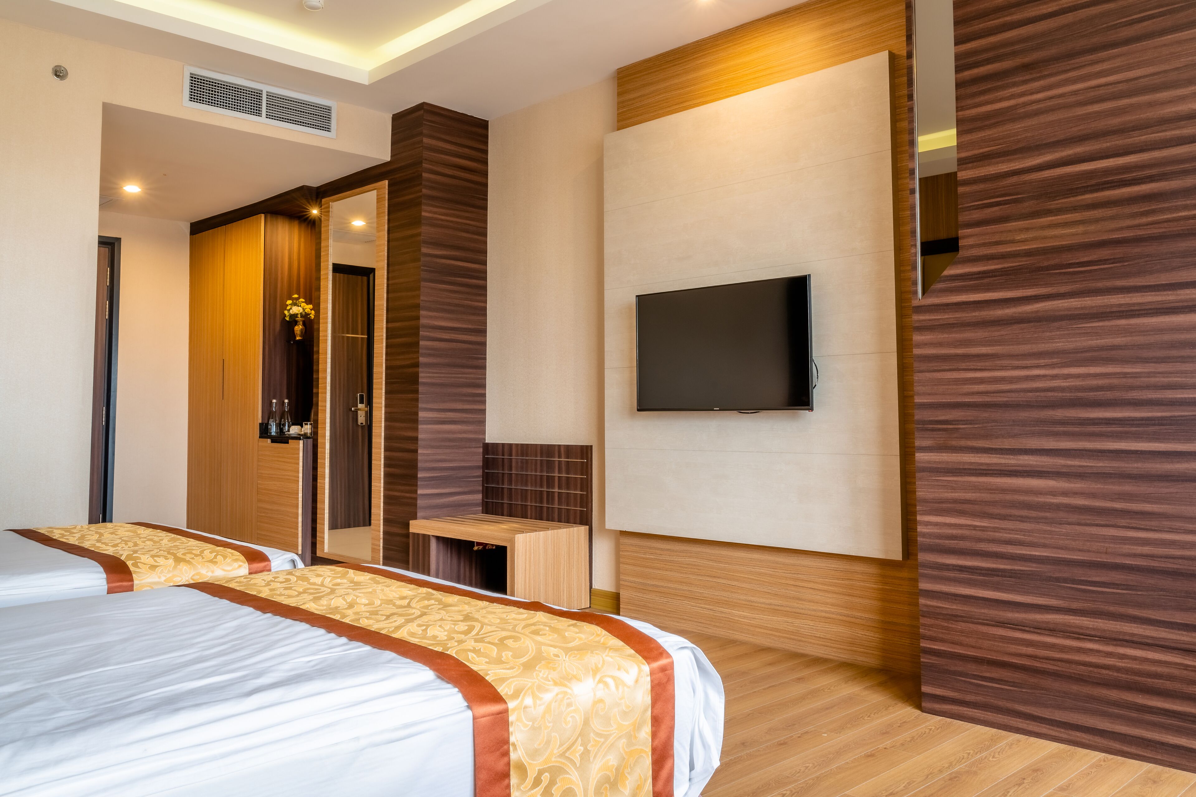 A hotel room with two beds, a TV mounted on the wall, and a wooden accent wall.