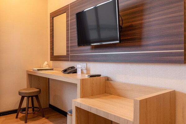 A hotel room with a wooden desk, a television mounted on the wall, a telephone, and a trash can. - M One Hotel (Batam)